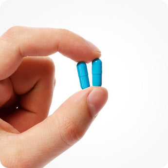 For Conceive Plus Men's Fertility Support and Fertility Lubricant Bundle product close-up showing two bright blue capsules held gently between thumb and forefinger, highlighting the supplement's compact size and ease of use against a white background.